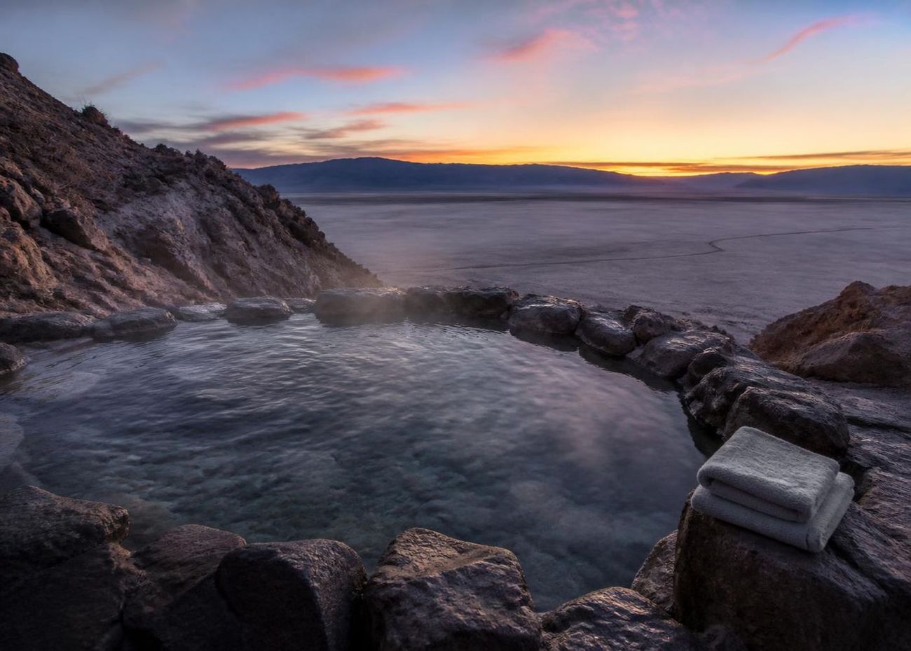 Steaming remote desert hot spring pool at twilight overlooking a dry lakebed